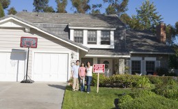 Family Standing Outside House With Real Estate Sign